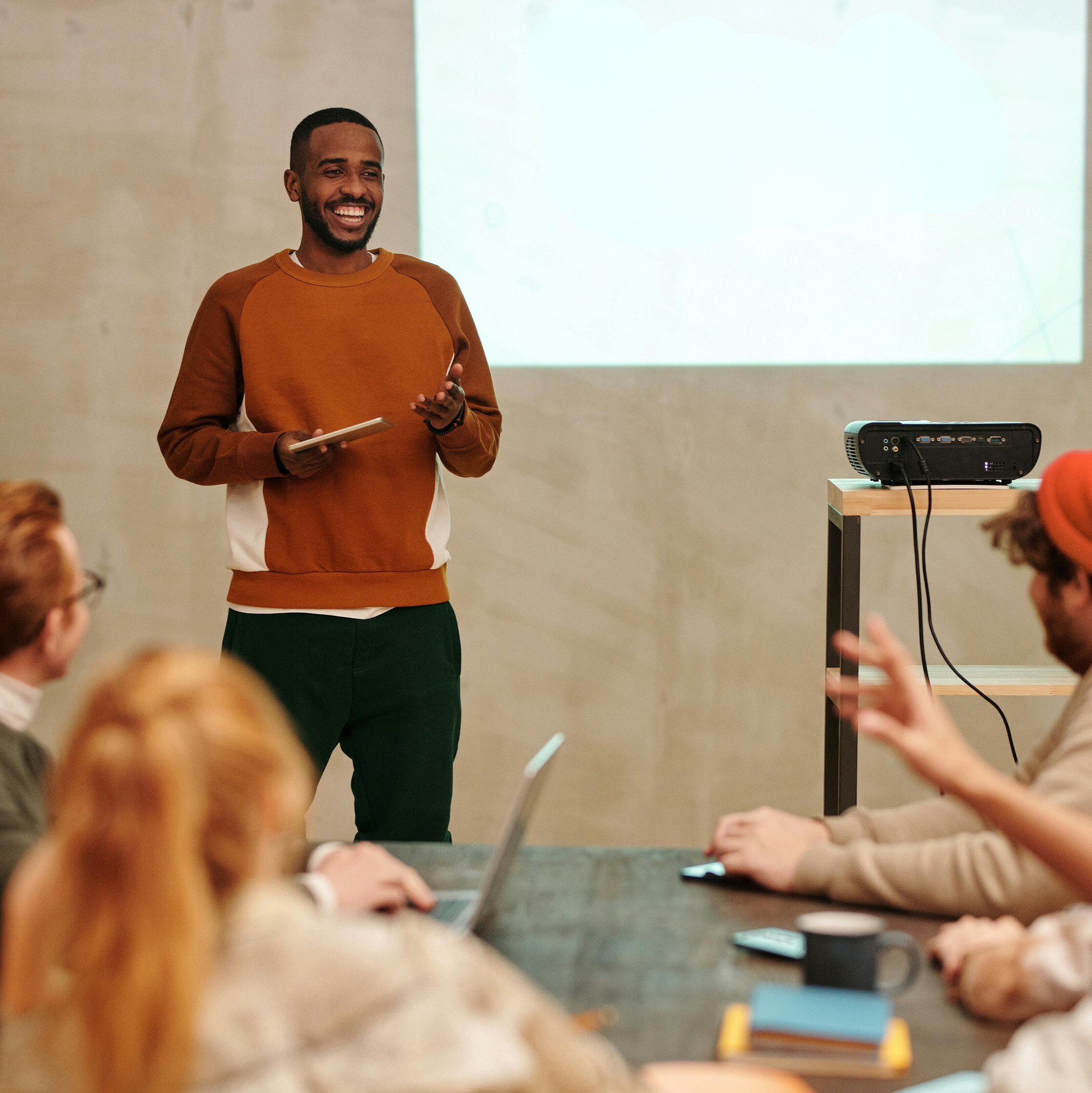a man standing in front of the room giving a presentation with a projector on in the background