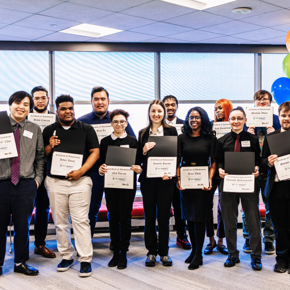 A group of Tech Impact students standing together with their program completion certificates. 